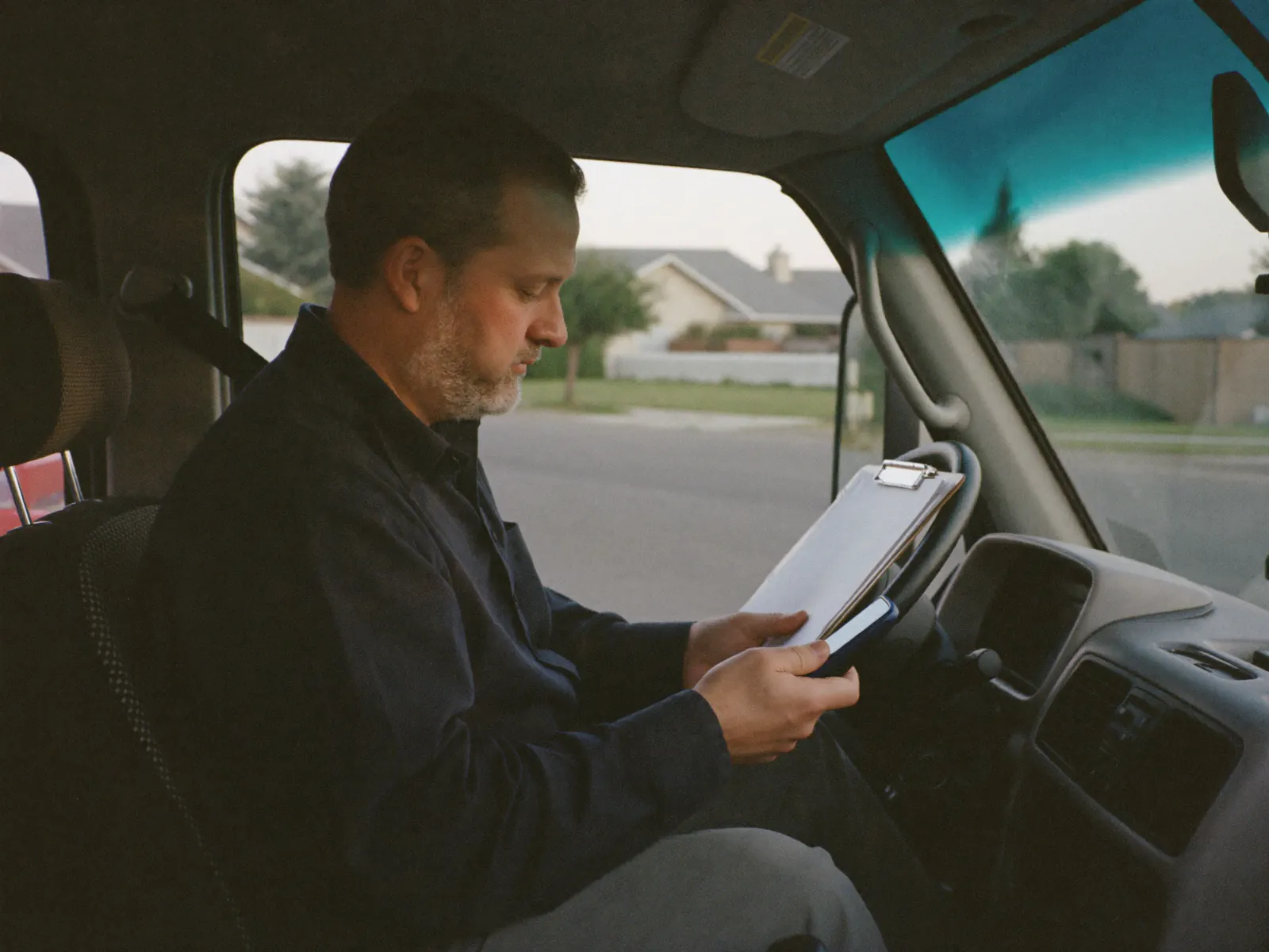 A business owner sits in his work truck, reviewing something on his phone.